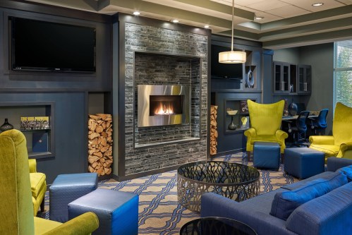 Modern lounge with a fireplace, blue and yellow furniture, and a stylish coffee table, creating a cozy atmosphere.