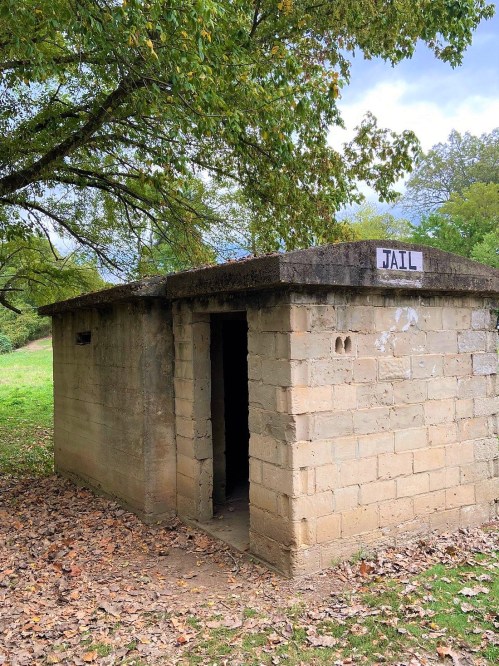 A small, stone building labeled "JAIL" surrounded by trees and fallen leaves.