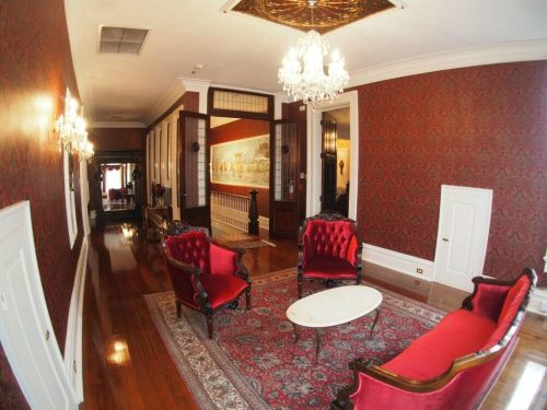 Elegant room with red wallpaper, vintage furniture, and a chandelier, featuring a marble coffee table and ornate decor.
