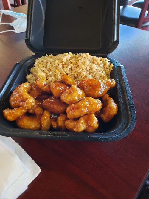 A takeout container with orange chicken and fried rice on a table.