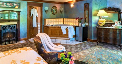 Cozy bedroom with a fireplace, a large tub, and elegant decor, featuring a plush chair and floral accents.