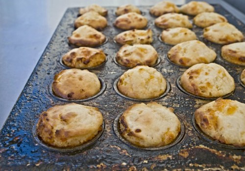A close-up of a muffin tray filled with golden-brown muffins, some slightly unevenly baked.