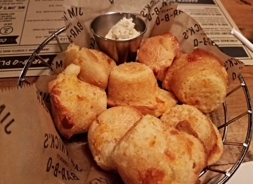 A basket of golden, cheesy biscuits served with a small cup of creamy dip on a rustic table.