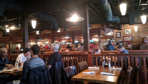 A bustling restaurant interior with wooden tables, patrons dining, and festive decorations in a warm atmosphere.