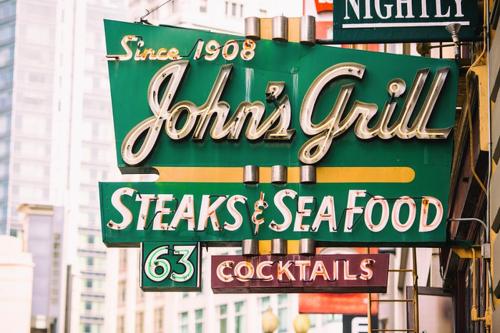 Vintage sign for John's Grill, featuring "Steaks & Sea Food," "Cocktails," and the year "Since 1908."
