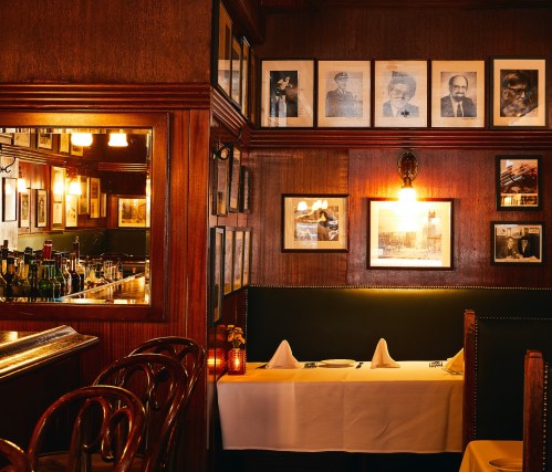 Cozy restaurant interior with wooden walls, framed photos, and a neatly set table with white linens.