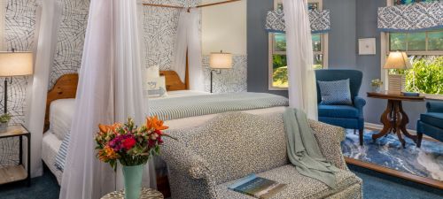 Cozy bedroom with a four-poster bed, floral decor, and a seating area, featuring soft lighting and blue accents.