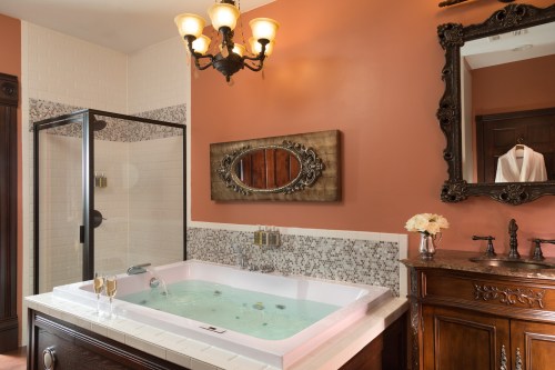 Luxurious bathroom featuring a jetted tub, shower, elegant mirror, and warm-toned walls with decorative tiles.