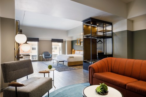 Modern hotel room featuring a bed, seating area, and large windows with natural light. Stylish decor and furnishings.