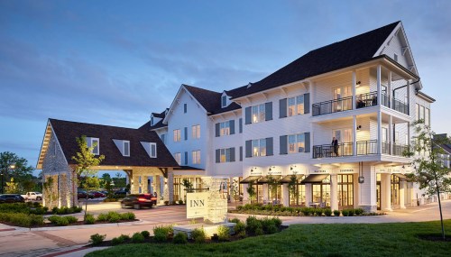A modern inn with a welcoming entrance, outdoor seating, and soft evening lighting, surrounded by greenery.
