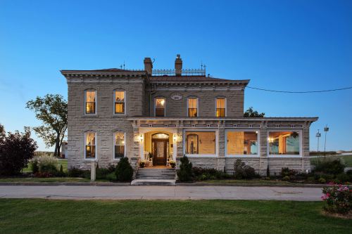 A historic two-story house with large windows, a porch, and a well-maintained garden, set against a twilight sky.