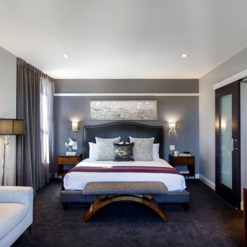 Modern hotel room featuring a queen bed, stylish decor, and soft lighting, with a cozy seating area and large windows.