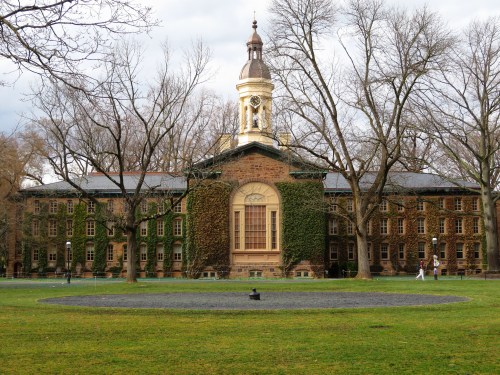 Historic building with ivy-covered walls, a clock tower, and a circular lawn, surrounded by bare trees.