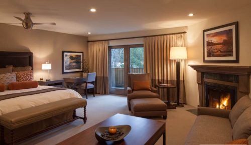 Cozy hotel room featuring a fireplace, king bed, seating area, and large windows with natural light.