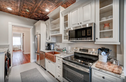 A modern kitchen featuring white cabinets, stainless steel appliances, and a decorative ceiling.