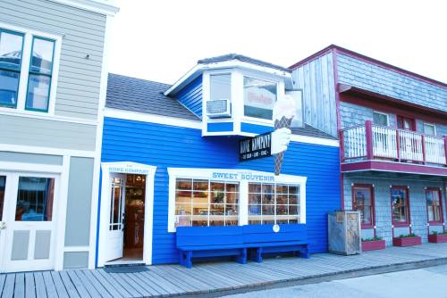 A blue building with an ice cream cone sign, featuring a shop window and a bench outside.