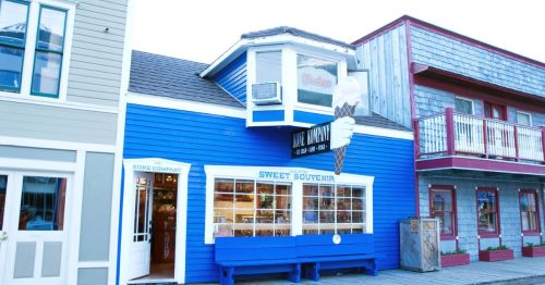 A blue building with an ice cream cone sign, featuring a shop window and a bench outside, surrounded by colorful structures.