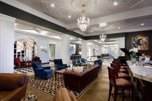 Elegant hotel lobby featuring plush seating, a grand piano, and ornate chandeliers, with a stylish bar area.