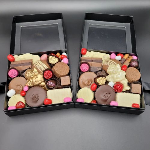 Two black boxes filled with an assortment of chocolates, candies, and decorative sweets in various shapes and colors.
