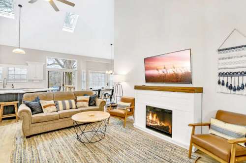 Cozy living room with a fireplace, modern decor, and large windows, featuring a sofa and stylish armchairs.