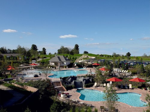 A scenic view of a resort pool area with multiple pools, lounge chairs, and red umbrellas under a clear blue sky.
