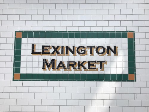 Sign for Lexington Market, featuring bold lettering on a tiled background with green and orange accents.
