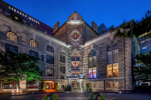 Historic stone building with large windows, illuminated at dusk, featuring a circular emblem above the entrance.
