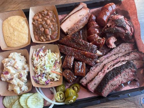 A platter of assorted barbecue meats, including brisket, sausage, and ribs, served with sides of beans, coleslaw, and pickles.