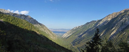 A panoramic view of a lush green valley surrounded by steep mountains under a clear blue sky.