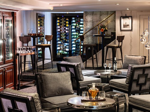 A stylish lounge with modern seating, a wine display, and elegant decor, creating a cozy atmosphere for relaxation.