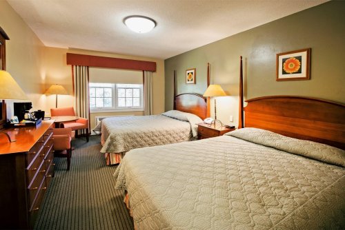 A cozy hotel room with two beds, a chair, a dresser, and a window with natural light. Decorated with floral art.
