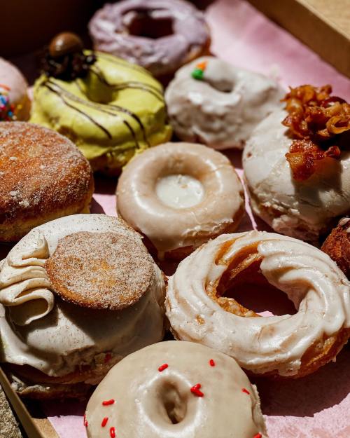A variety of colorful donuts in a box, featuring different toppings and flavors, on a pink paper lining.