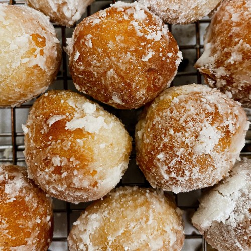 A close-up of golden, powdered sugar-coated doughnut holes on a wire rack.