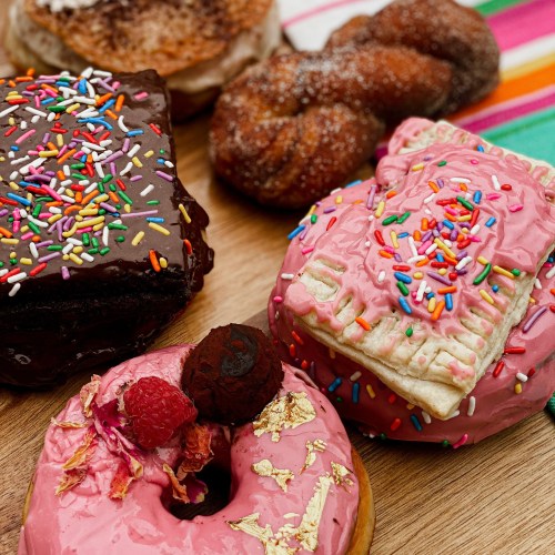 A colorful assortment of donuts, including chocolate, pink frosted, and sprinkled varieties, arranged on a wooden surface.