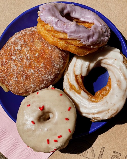 A blue plate with four assorted donuts: a cinnamon sugar, a purple frosted, a glazed, and a sprinkles-topped donut.