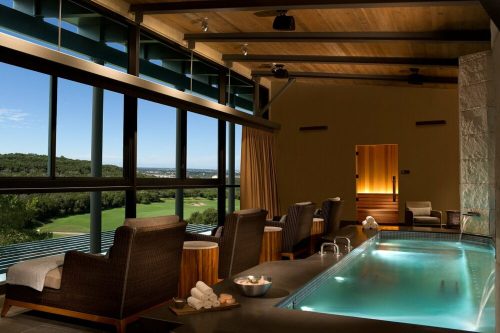 A serene spa interior with a pool, lounge chairs, and large windows overlooking a scenic landscape.