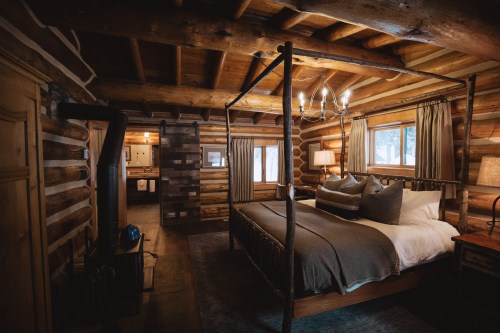Cozy log cabin interior featuring a four-poster bed, warm lighting, and rustic wooden accents.
