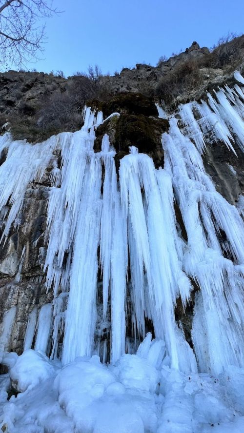 Icicles hanging from a rocky cliff, with a clear blue sky above and snow-covered ground below.