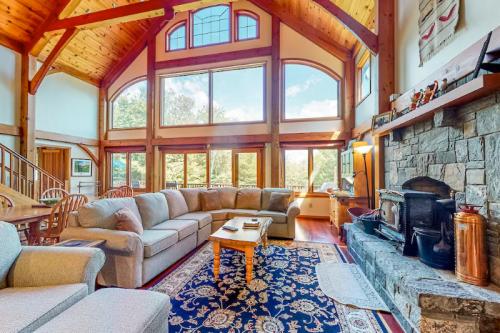 Spacious living room with high wooden ceilings, large windows, a stone fireplace, and cozy furniture.