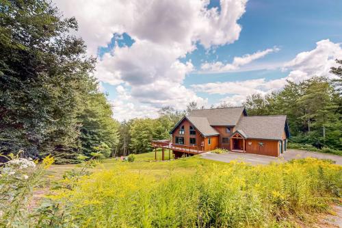 A modern house surrounded by trees and greenery, set against a bright blue sky with fluffy clouds.