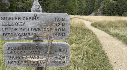 Wooden signpost with trail distances to Shipler Cabins, Lulu City, Little Yellowstone, and more, set in a grassy landscape.