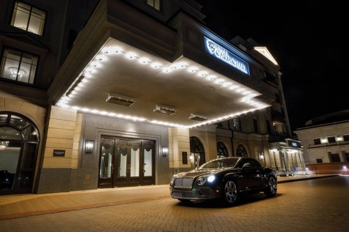A luxury car parked in front of an elegant hotel entrance at night, illuminated by bright lights.