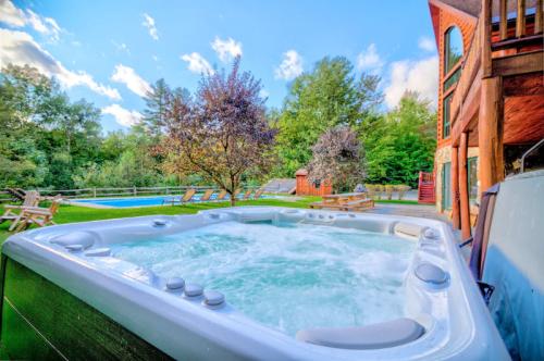 A hot tub in a backyard with trees, a pool, and a wooden house under a blue sky with fluffy clouds.