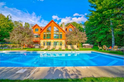 A large wooden house with a pool and lounge chairs, surrounded by trees and blue skies.