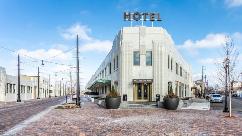 A modern hotel building with a "HOTEL" sign, surrounded by a brick-paved street and decorative planters.