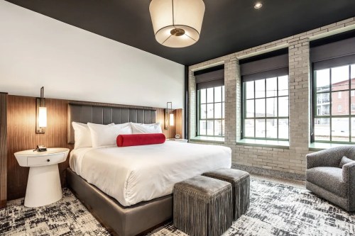 Modern hotel room featuring a king-sized bed, large windows, and stylish furnishings in neutral tones.