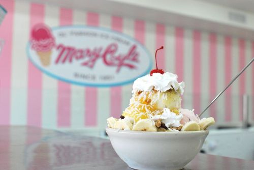 A delicious ice cream sundae topped with whipped cream and a cherry, set against a pastel pink striped background.
