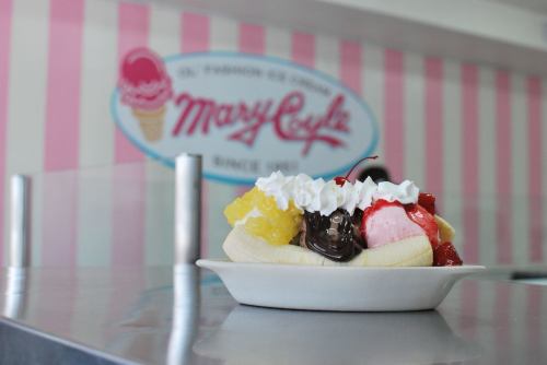 A colorful banana split topped with whipped cream, cherries, and various ice cream flavors, set against a pastel backdrop.