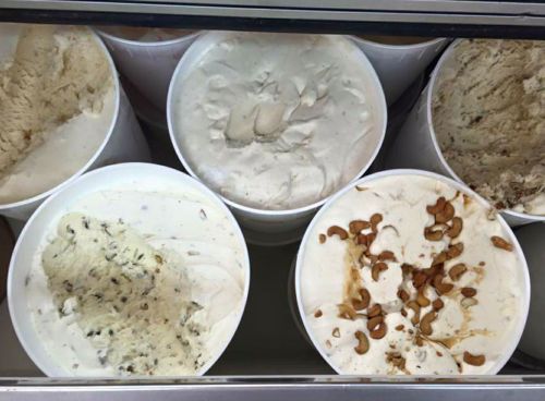 A variety of ice cream tubs in a freezer, featuring different flavors and toppings, including nuts.