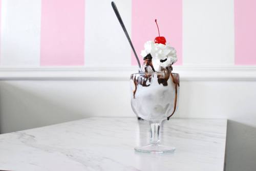 A delicious ice cream sundae topped with whipped cream and a cherry, served in a glass on a marble table.